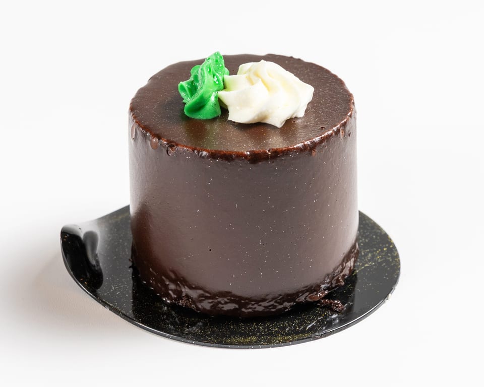 A small, round chocolate cake with green and white frosting on top, on a black plate.