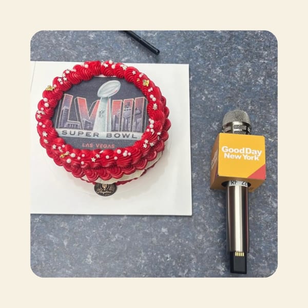 Super Bowl-themed cake with red frosting and a "Good Day New York" microphone on a counter.