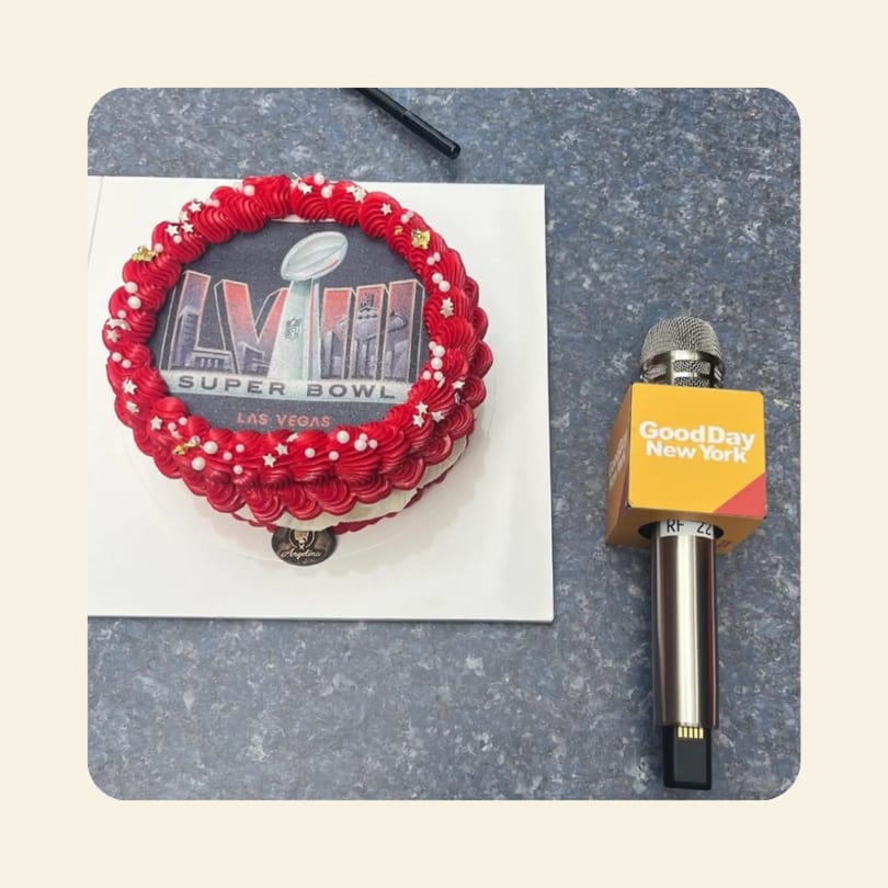 Super Bowl-themed cake with red frosting and a "Good Day New York" microphone on a counter.