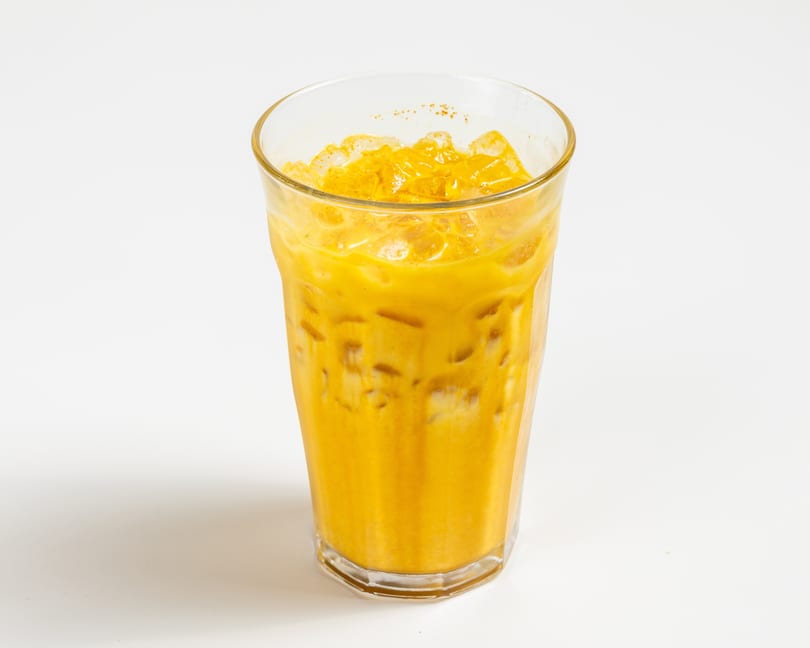 Iced Thai tea in a tall glass with ice, garnished with a sprinkle of spice.