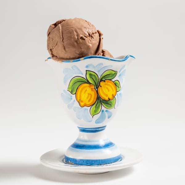 Two scoops of chocolate ice cream in a decorative white, blue, and yellow ceramic cup.