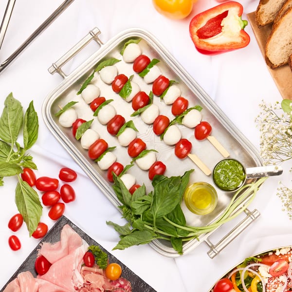 Overhead view of a buffet spread with salads, caprese skewers, charcuterie, and fresh vegetables.
