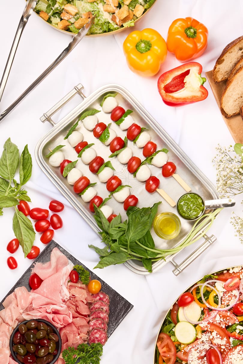 Overhead view of a buffet spread with salads, caprese skewers, charcuterie, and fresh vegetables.