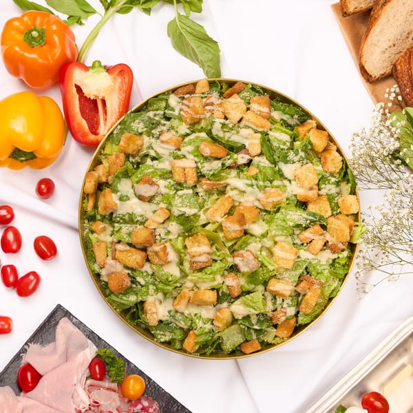 Overhead view of a buffet spread with Caesar salad, Greek salad, charcuterie, and caprese skewers.