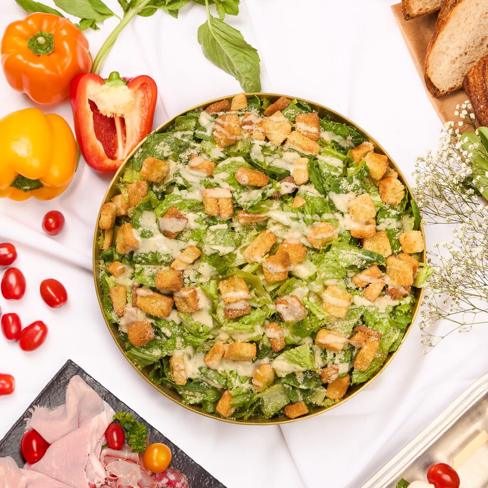 Overhead view of a buffet spread with Caesar salad, Greek salad, charcuterie, and caprese skewers.