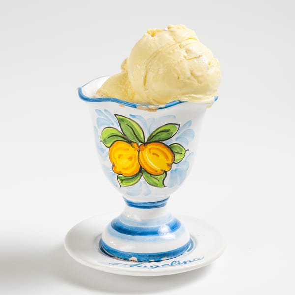 Scoops of yellow ice cream in a hand-painted ceramic cup with lemons and blue stripes.