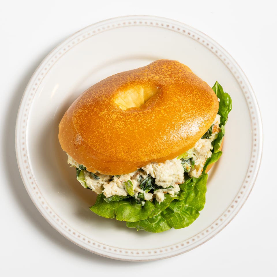 Bagel sandwich with chicken salad and lettuce on a white plate with a decorative rim.