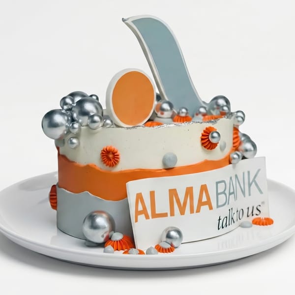 A decorative cake in orange, white, and silver with "ALMA BANK talk to us" sign.