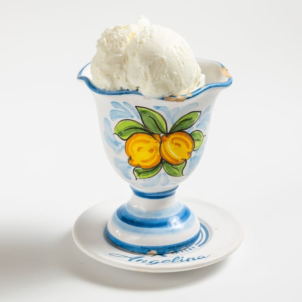 Two scoops of vanilla ice cream in a decorative ceramic cup with painted lemons and blue stripes.