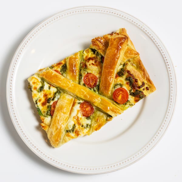 Savory pastry tart with pesto, melted cheese, and cherry tomatoes on a white plate.