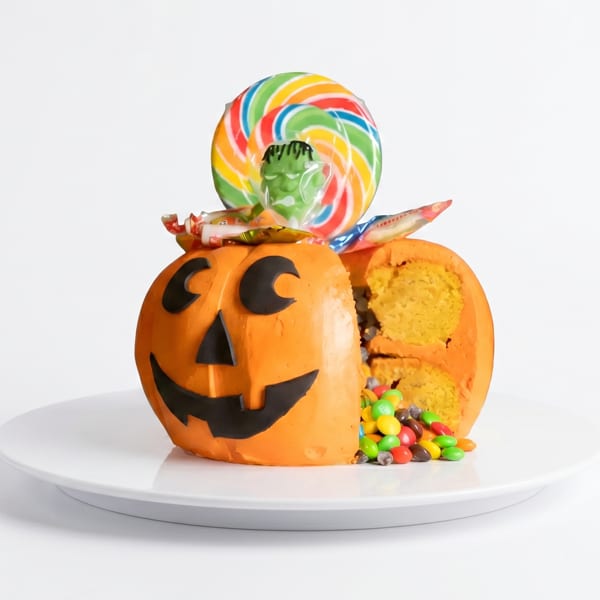 A Halloween pumpkin cake, cut open to reveal candy and cake inside, with a lollipop on top.