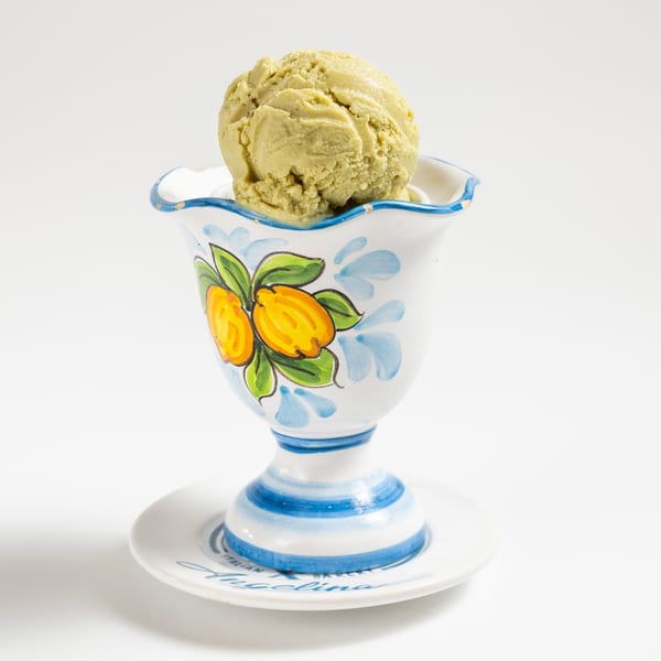 A scoop of pistachio gelato in a decorative white, blue, and yellow ceramic cup.