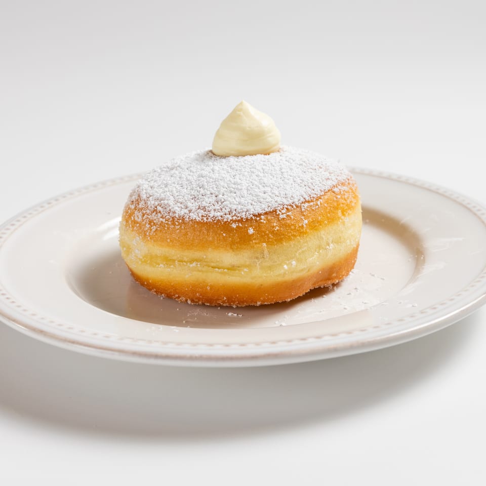 A powdered sugar donut with a dollop of cream on top, served on a white plate.