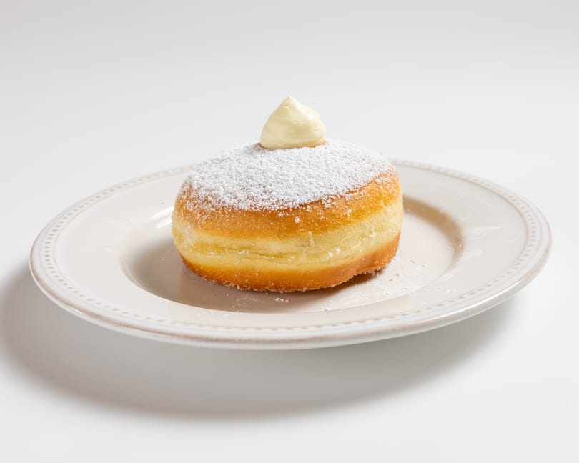 A powdered sugar donut with a dollop of cream on top, served on a white plate.
