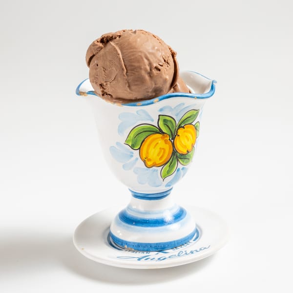 A scoop of chocolate ice cream in a decorative white cup with blue and yellow lemon designs.