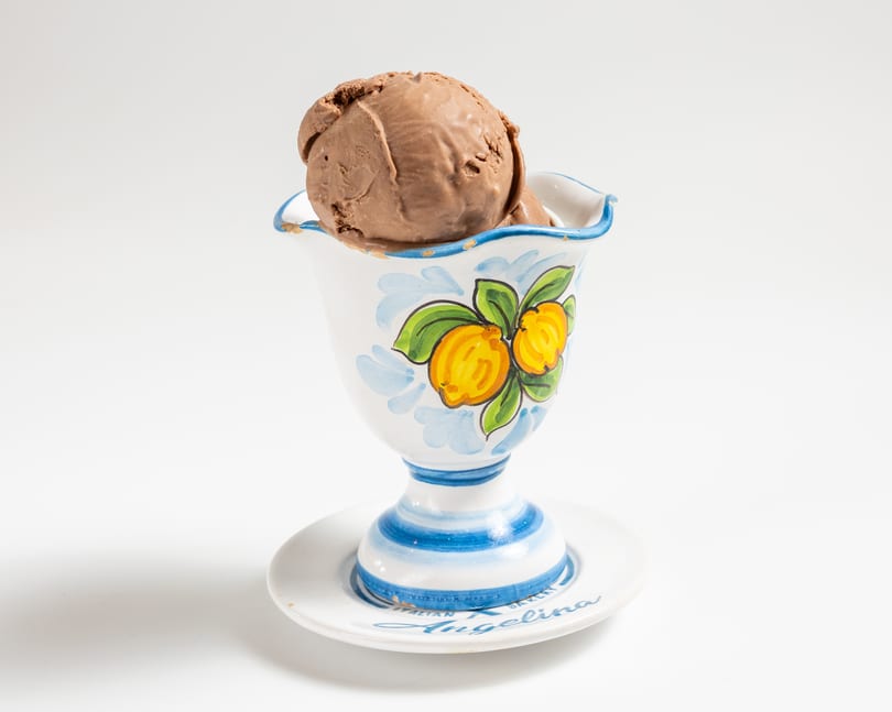 A scoop of chocolate ice cream in a decorative white cup with blue and yellow lemon designs.