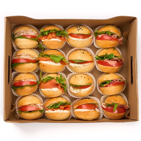 An overhead view of a cardboard box filled with 16 mini sandwiches, each in a white paper cup.