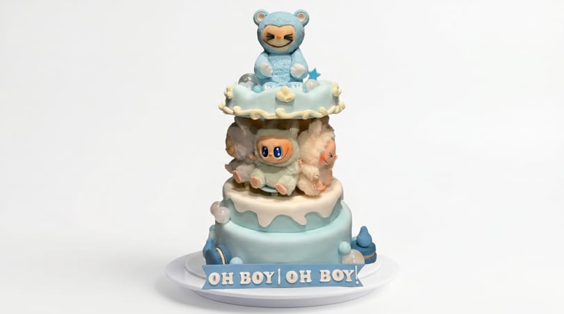 A three-tiered baby shower cake with blue and white frosting, topped with cute animal figurines.