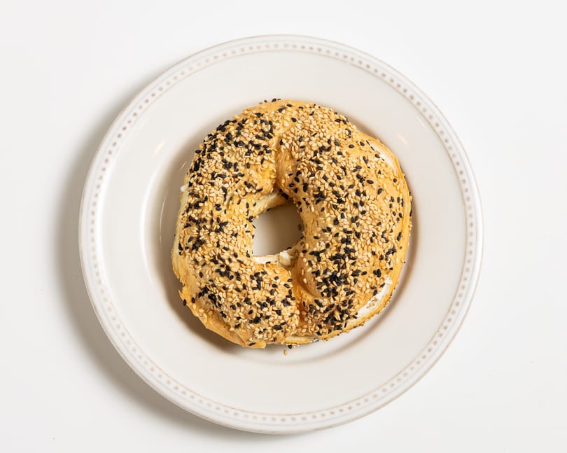 Everything bagel with cream cheese on a white plate, shot from above.