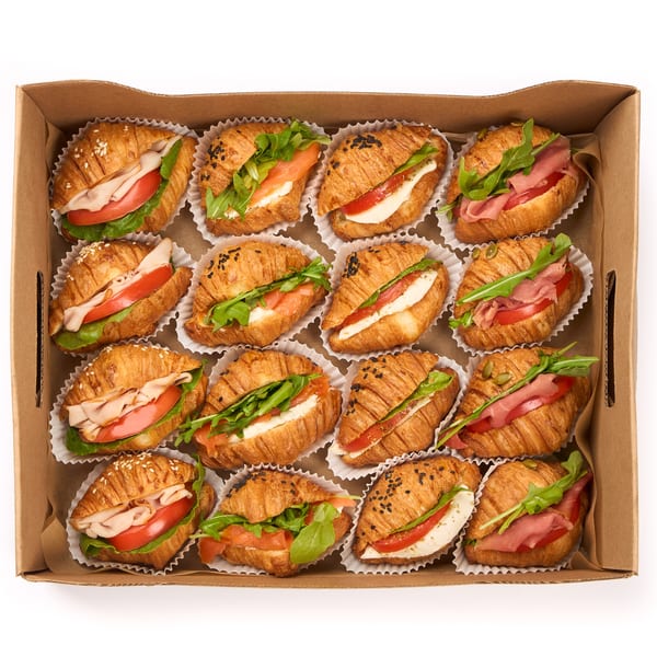A cardboard box filled with 15 mini croissant sandwiches, each with various fillings.
