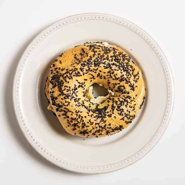 A sesame bagel with cream cheese filling, served on a white plate.