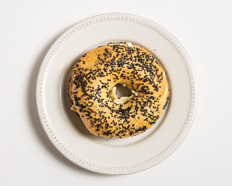 A sesame bagel with cream cheese filling, served on a white plate.