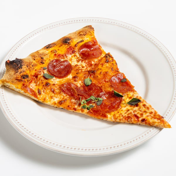A single slice of pepperoni pizza with fresh oregano on a white plate.
