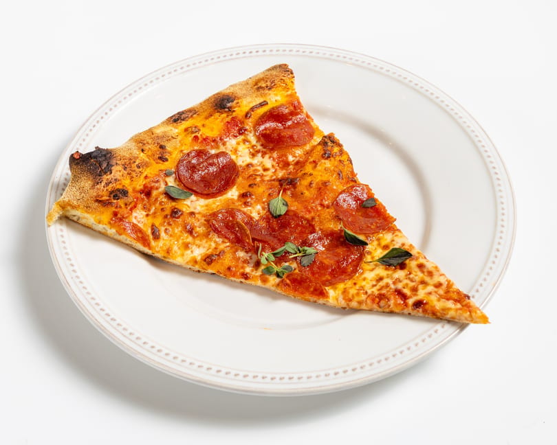 A single slice of pepperoni pizza with fresh oregano on a white plate.