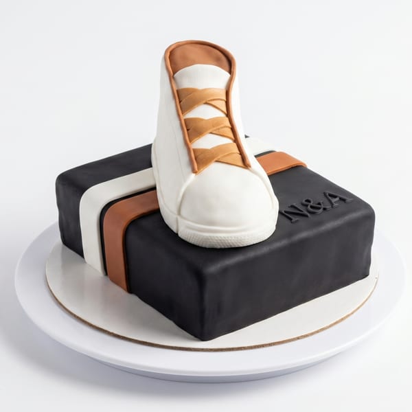 A black square cake with white and brown stripes, topped with a white and brown sneaker.
