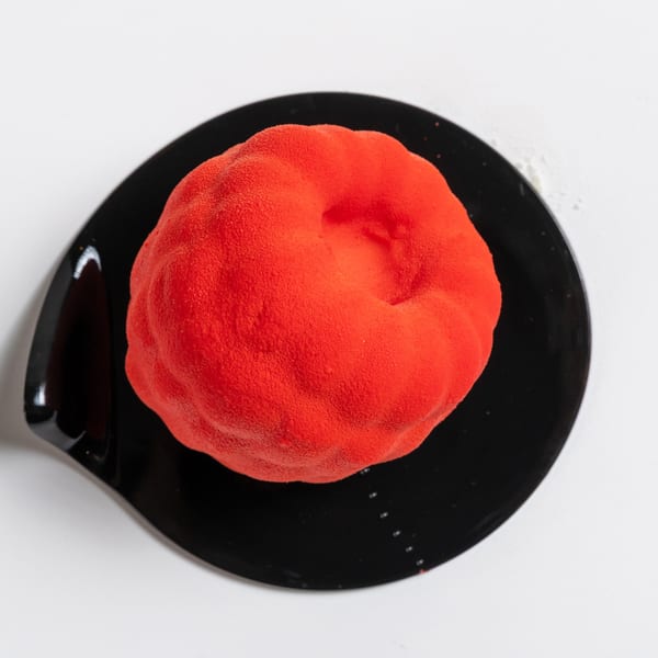 Vibrant red dessert with a textured, velvety finish, served on a sleek black plate.