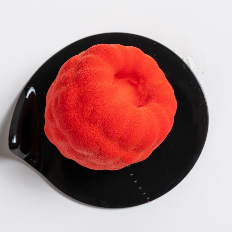 Vibrant red dessert with a textured, velvety finish, served on a sleek black plate.