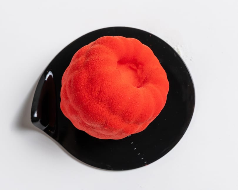 Vibrant red dessert with a textured, velvety finish, served on a sleek black plate.