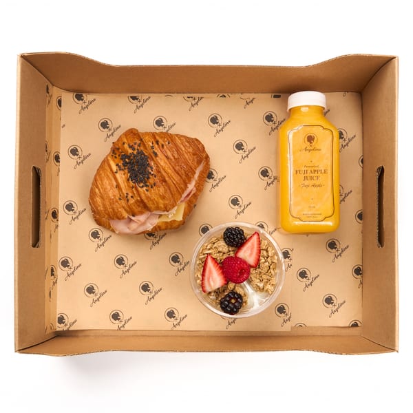 Boxed breakfast with a ham and cheese croissant, fruit and granola parfait, and Fuji apple juice in an Angelina box.