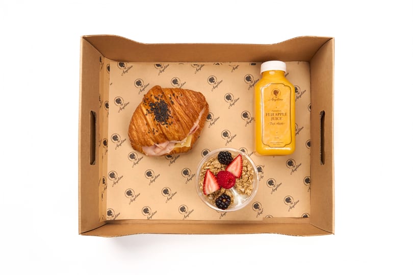 Boxed breakfast with a ham and cheese croissant, fruit and granola parfait, and Fuji apple juice in an Angelina box.