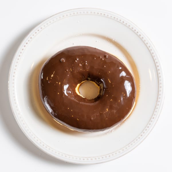 A chocolate-glazed donut with a hole in the center, resting on a white plate.