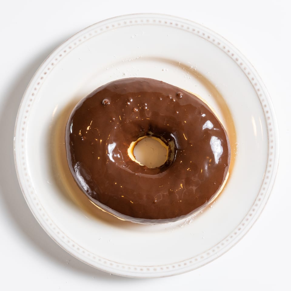 A chocolate-glazed donut with a hole in the center, resting on a white plate.