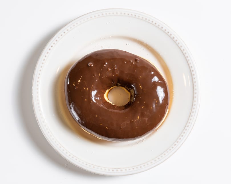 A chocolate-glazed donut with a hole in the center, resting on a white plate.
