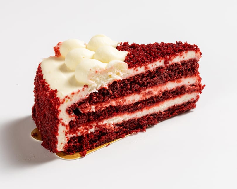 A slice of red velvet cake with multiple layers of red cake and white cream cheese frosting.