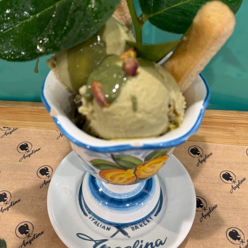 Pistachio gelato with a ladyfinger in a decorative cup on an Angelina Italian Bakery coaster.