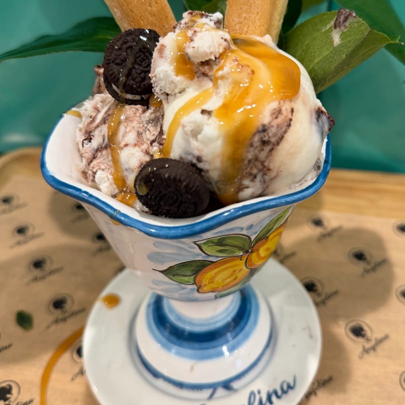 Cookies and cream gelato with caramel drizzle, wafer sticks, and mini Oreos in a decorative cup.