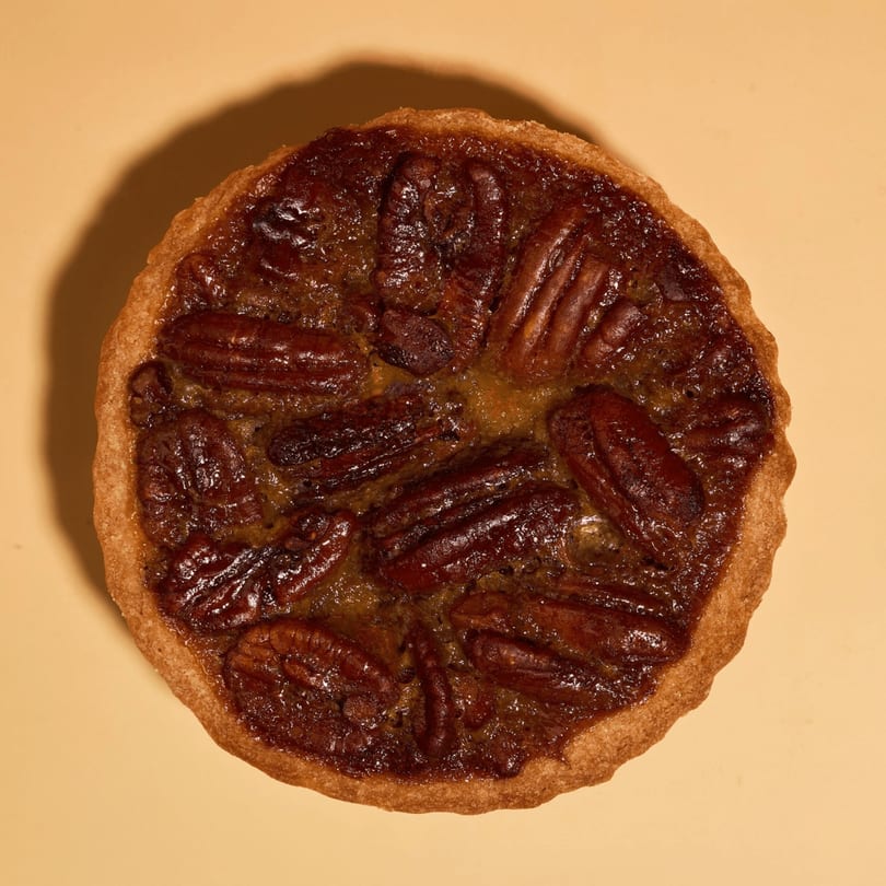 A whole pecan pie with a golden crust and glossy, dark pecan filling on a light background.