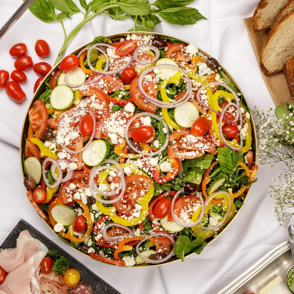 Large salad with tomatoes, peppers, zucchini, onions, olives, and feta cheese.
