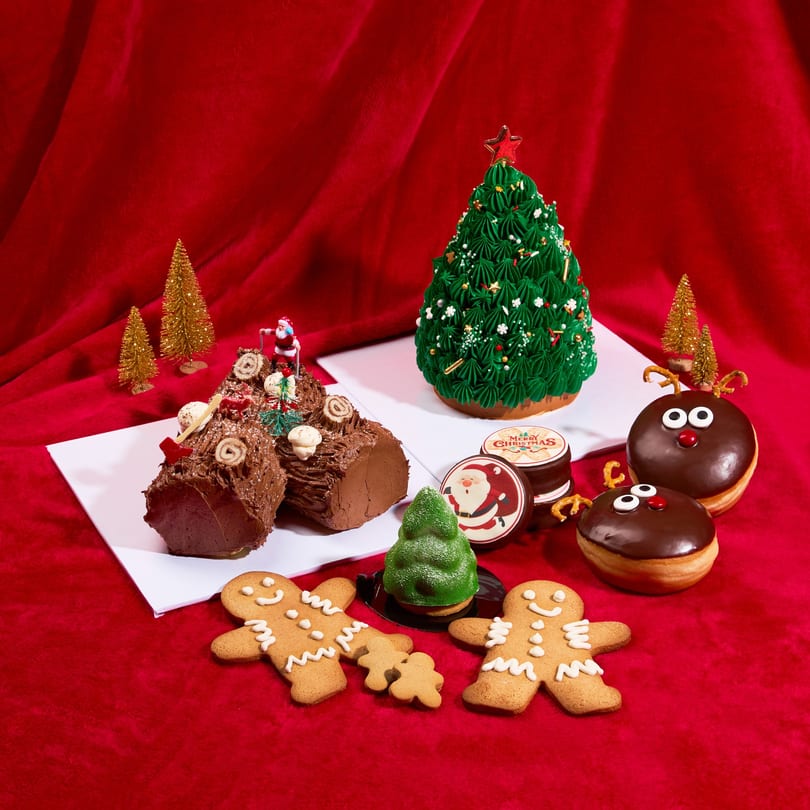 A festive display of Christmas desserts, including chocolate yule logs, gingerbread men, and reindeer donuts.