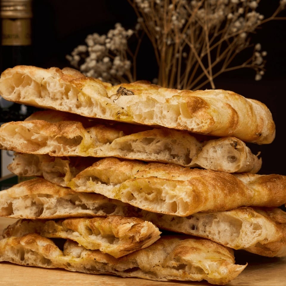 A stack of golden-brown focaccia bread slices with visible air pockets on a wooden surface.