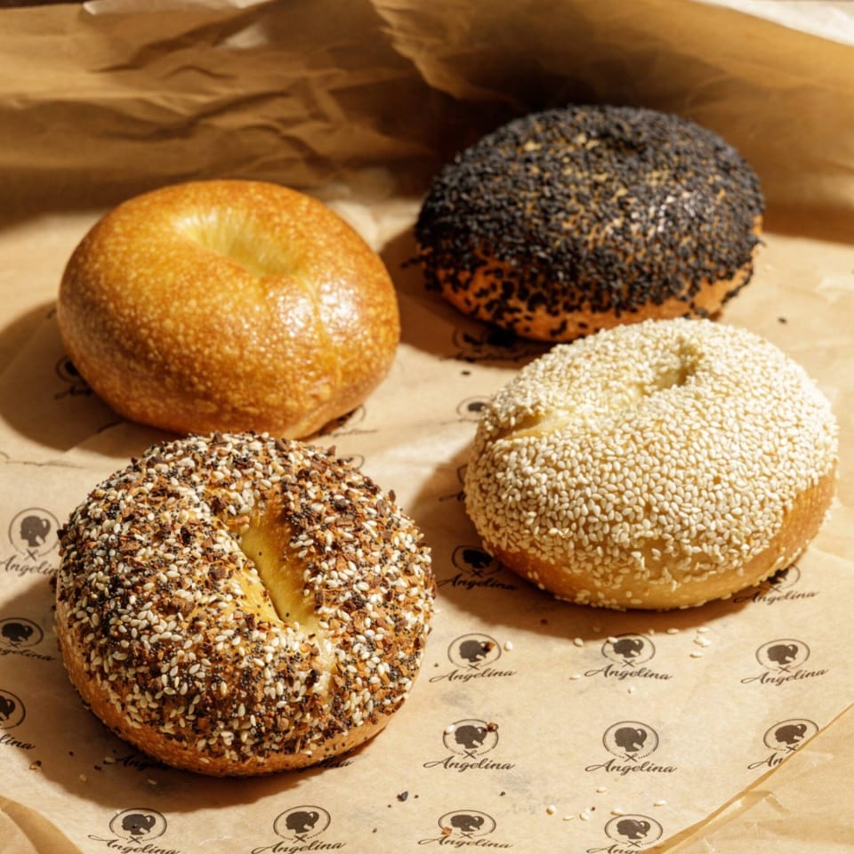 Four bagels, plain, black sesame, everything, and white sesame, on Angelina Bakery branded paper.