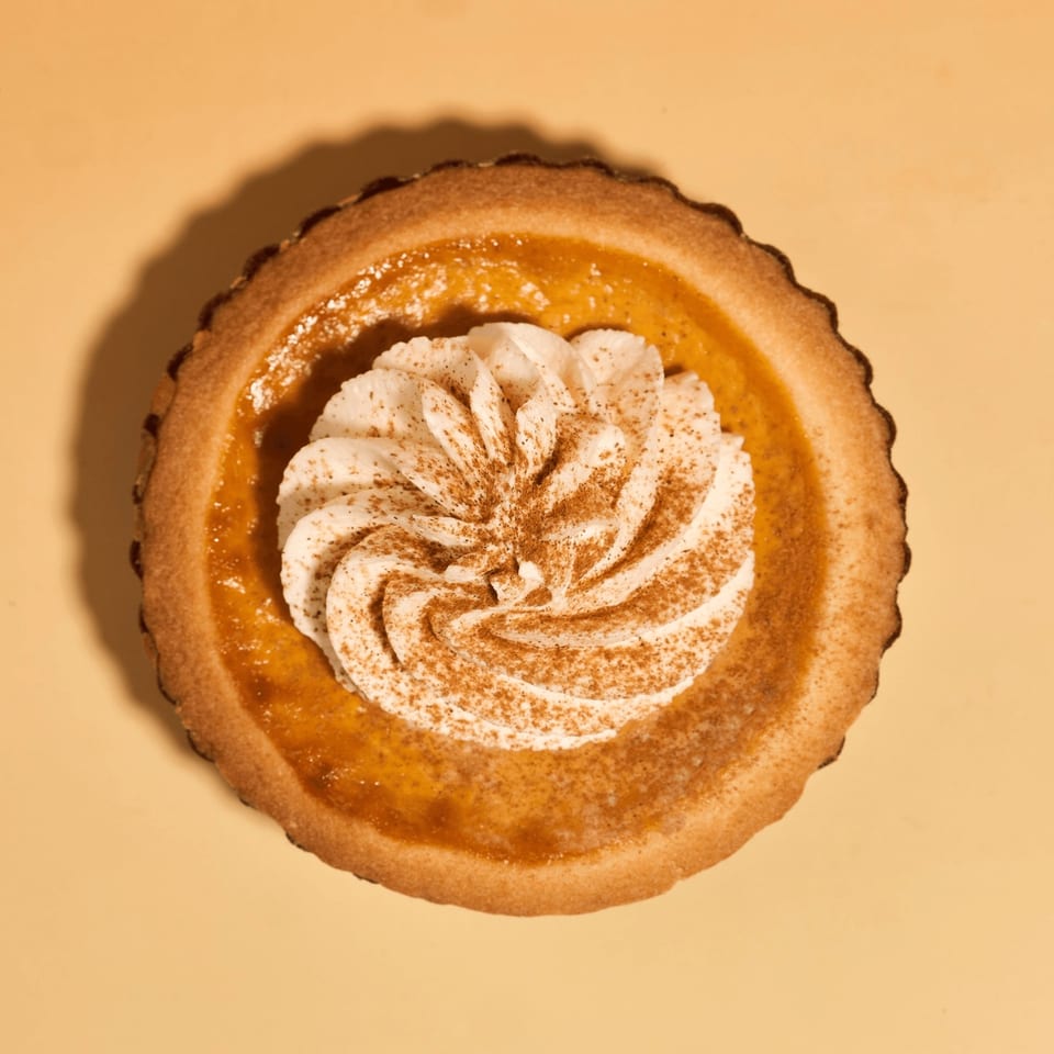 Overhead view of a pumpkin pie tart with whipped cream and cinnamon on a yellow background.