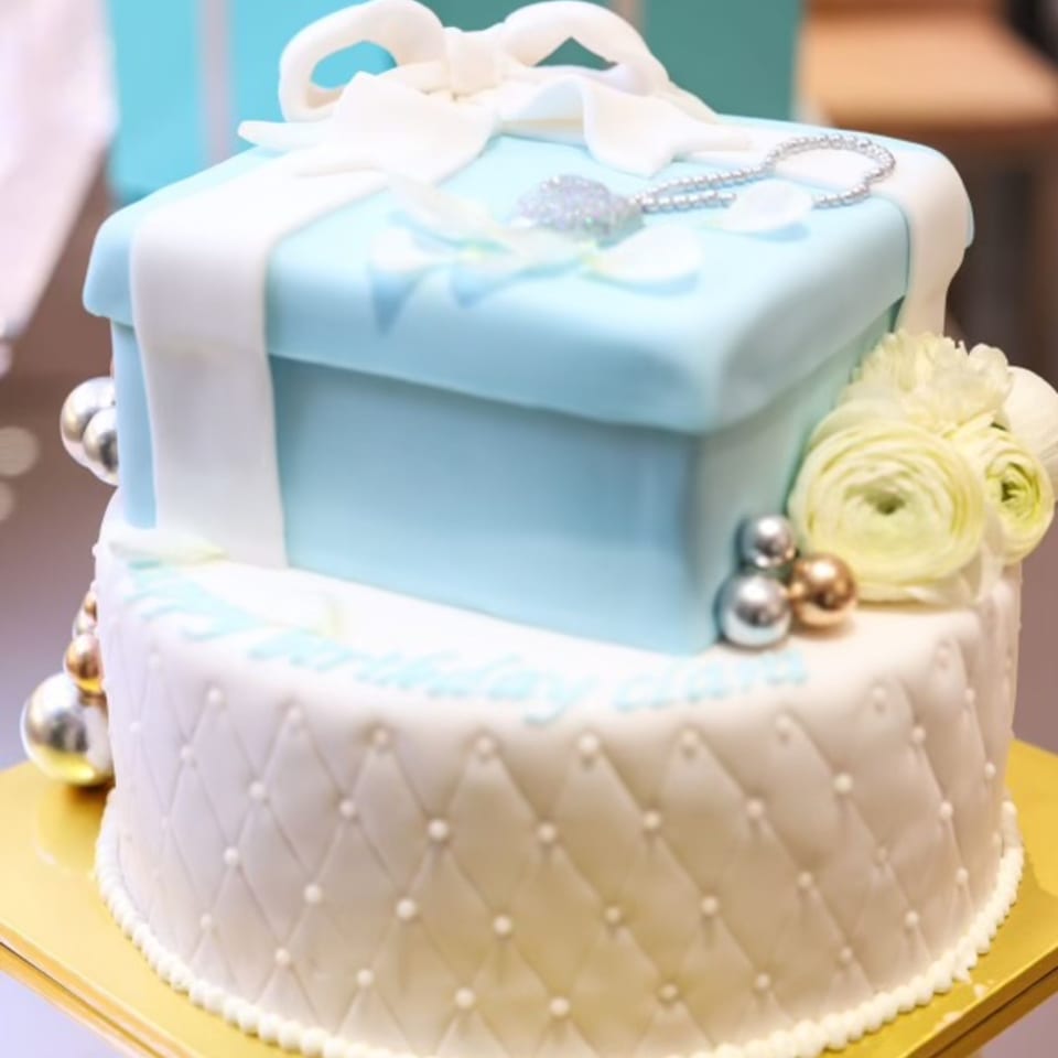 Two-tier cake with a light blue gift box on top and a white quilted bottom tier.