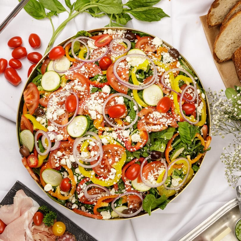 Large platter of colorful salad with tomatoes, peppers, zucchini, onions, olives, and feta cheese.