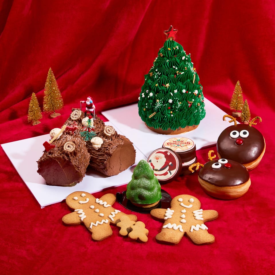 Christmas desserts including a Yule log, tree cake, gingerbread men, and reindeer donuts on red fabric.