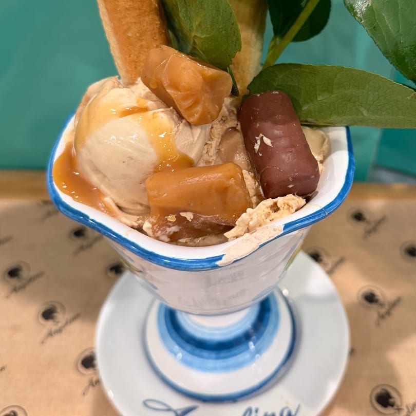 Caramel ice cream sundae with candy, cookies, and mint leaves in a blue and white bowl.